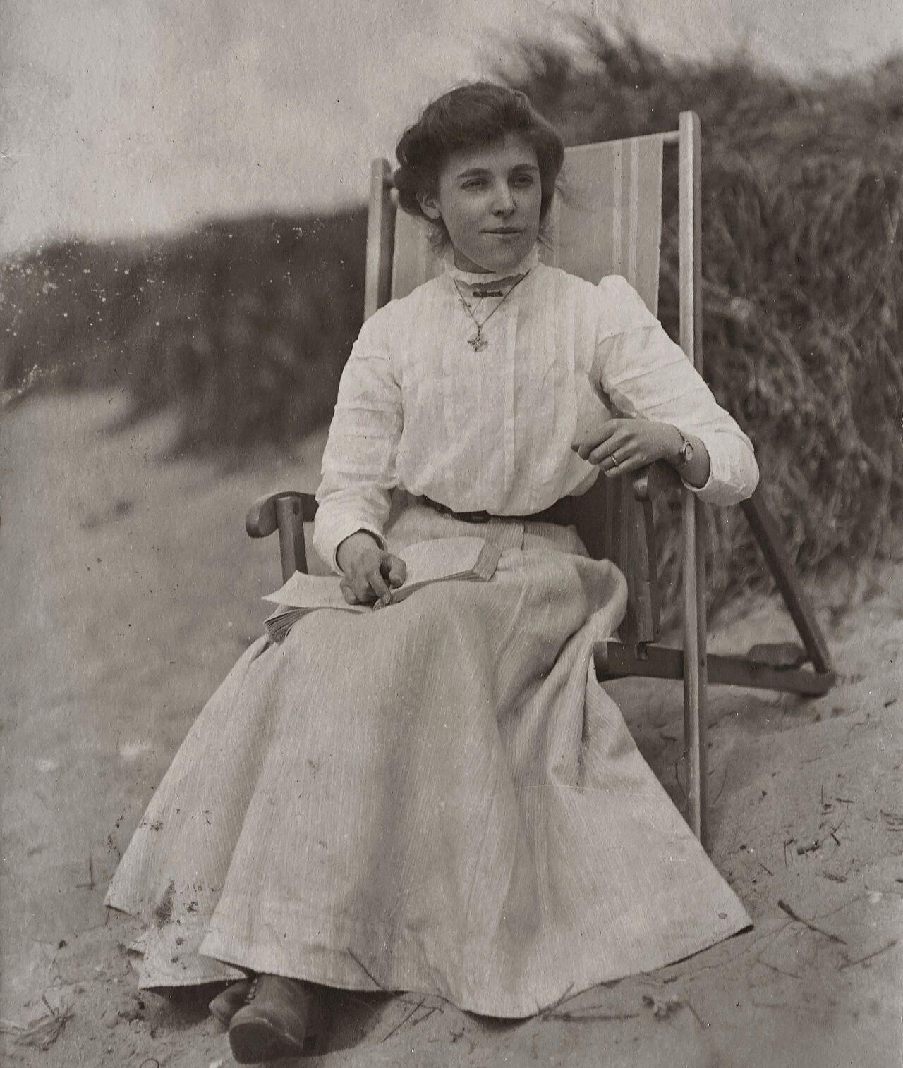 femme assise sur la plage – Vintage Femme sur une chaise de plage, un livre sur ses genoux, villégiature du début du XXᵉ siècle.
